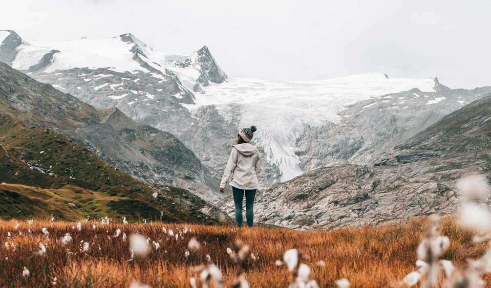 Wanderin genießt in einem weiten Almboden in Innergschlöss den Ausblick auf die schneebedeckten Gipfel.