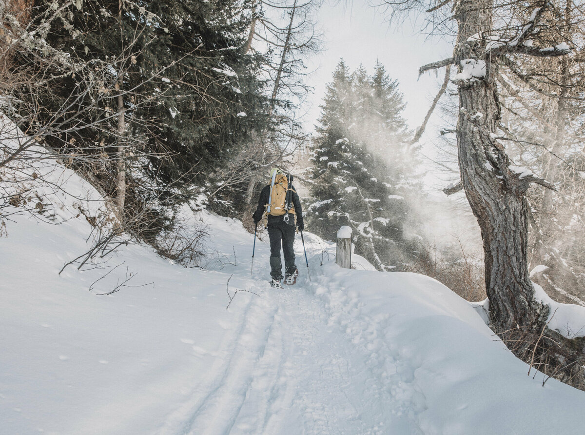 Winterwandern-Osttirol Ein Schneeschuwanderer mit gelbem Rucksack steigt durch einen verschneiten Wald in Osttirol.