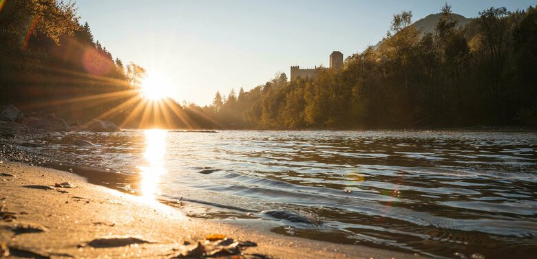 Das Ufer der Isel in der untergehenden Sonne. Im Hintergrund Blick auf das Schloss Bruck.
