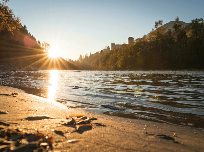 Das Ufer der Isel in der untergehenden Sonne. Im Hintergrund Blick auf das Schloss Bruck.