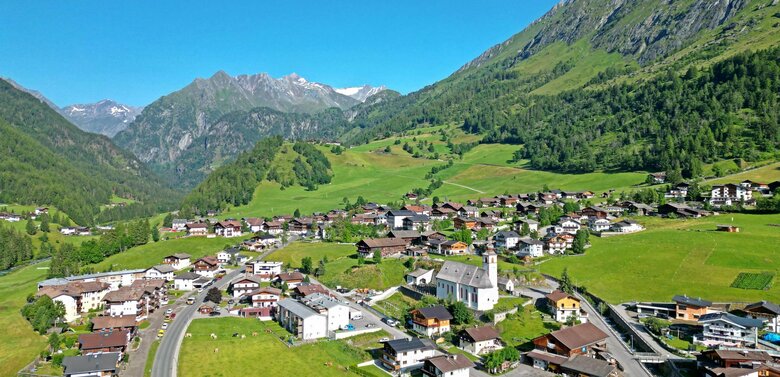 Blick von oben auf das Dorf Prägraten im Sommer. Im Hintergrund liegen noch Schneereste auf den Berggipfeln. In der Mitte ragt die Kirche empor.
