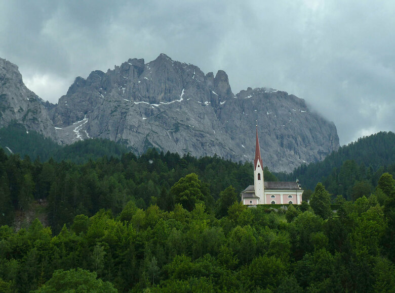 Lavant Die Kirche St. Ulrich in Lavant ragt aus dem dicht bewaldeten Hügel hervor. Im Hintergrund sieht man die Ausläufer der Lienzer Dolomiten.