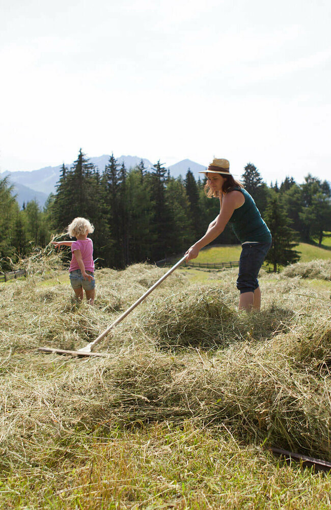 Eine Frau und zwei Kinder stehen auf dem Feld und rechen Heu.