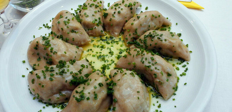 Osttiroler Schlipfkrapfen mit Schnittlauch und geschmolzener Butter auf einem weißen Teller angerichtet.