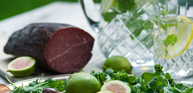 Frühstück Henkele in feine Scheiben aufgeschnitten und auf einer runden Platte angerichtet mit Feigen, Oliven und Rucola.