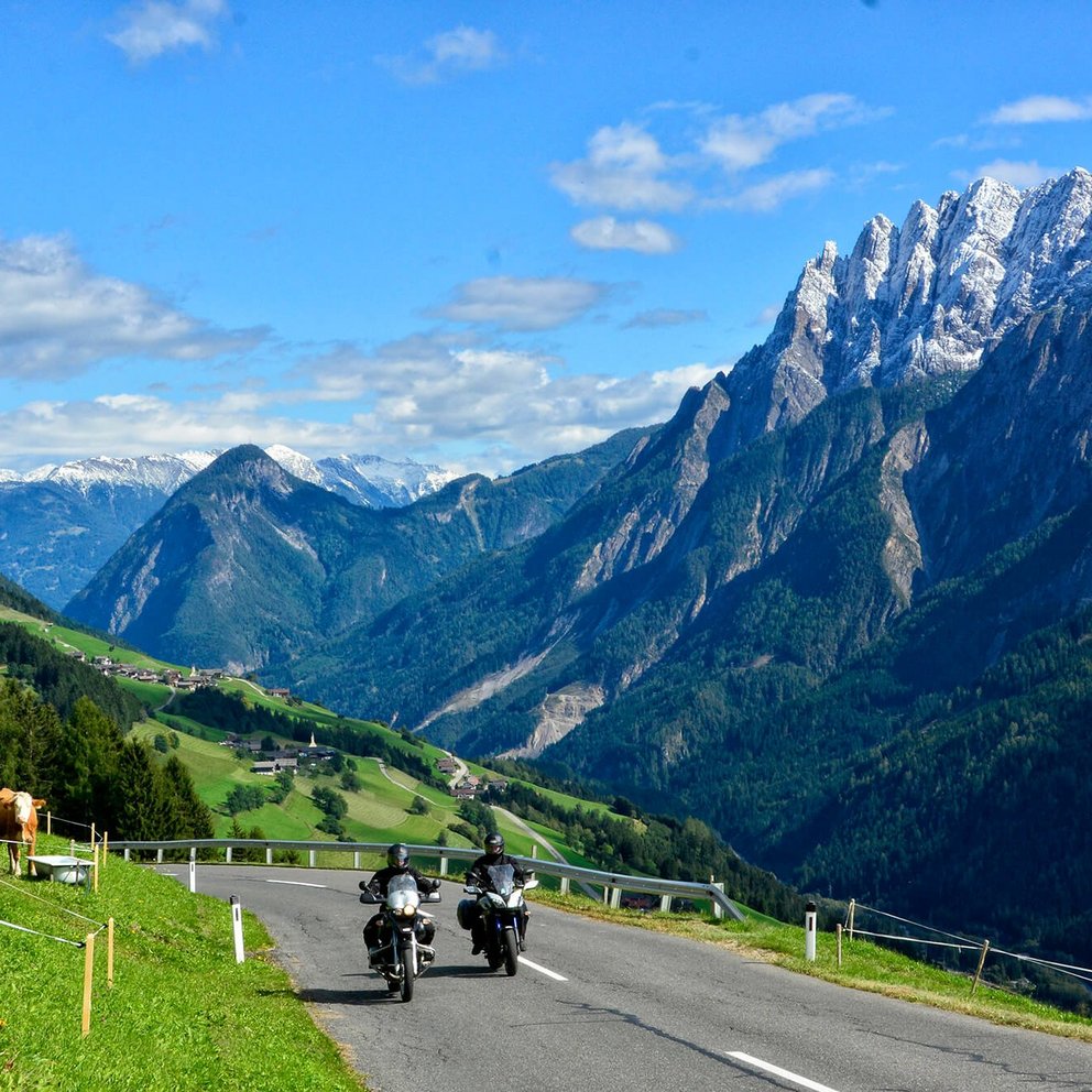 Zwei Motorradfahrer auf der Pustertaler Höhenstraße im Frühling. Grüne Wiesen im Tal und schneebedeckte Gipfel der Lienzer Dolomiten.