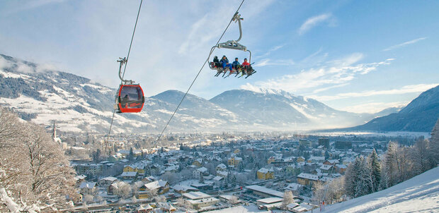 Sessel und rote Gondel schweben über die tief verschneite Winterlandschaft am Hochstein mit der Stadt Lienz im Hintergrund.