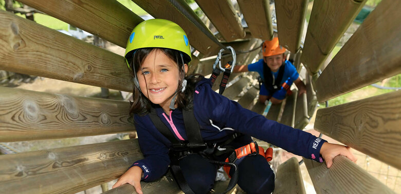 Zwei Kinder durchqueren die Holzröhren im Hochseilgarten Sillian