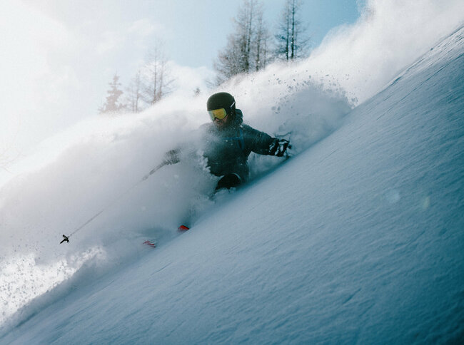 Ein Skitourenfahrer bei der Abfahrt von der Roten Wand im Defereggental. Er fährt durch Tiefschnee und Trägt Helm, Skibrille und Stöcke. 