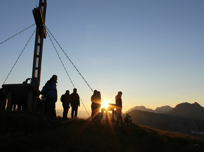 Silhouetten einer Gruppe von Menschen vor dem Sonnenaufgang am Golzentipp Obertilliach
