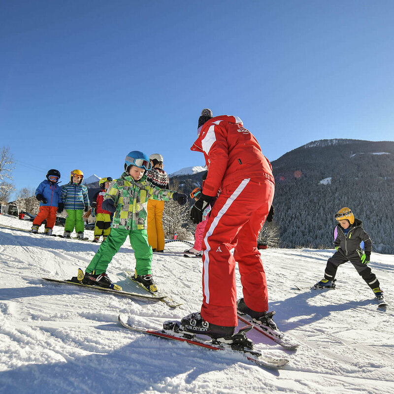 Ein rot gekleideter Skilehrer mit mehreren Kindern bei Traumwetter am Fellach Lift in Virgen.