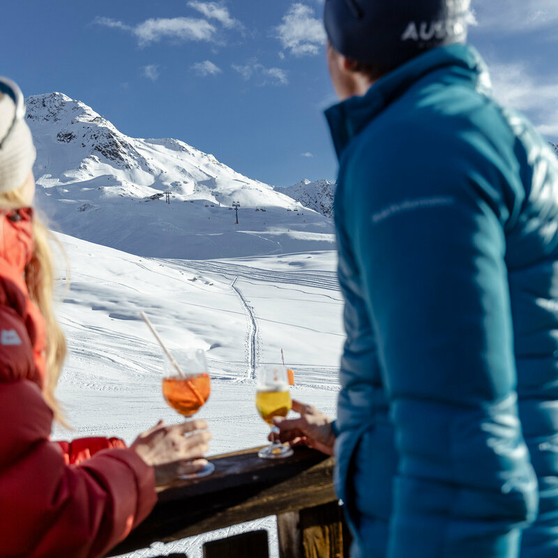 Skifahrer genießen ein Erfrischungsgetränk mit Blick auf die Pisten des Skizentrum St. Jakob i. D..