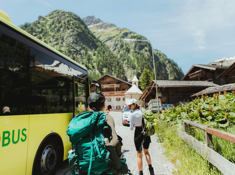 Zwei Wanderer steigen aus dem gelben Linienbus der ÖBB aus, im Hintergrund steht der traditionsreiche Gasthof „Matreier Tauernhaus“ in Matrei in Osttirol.