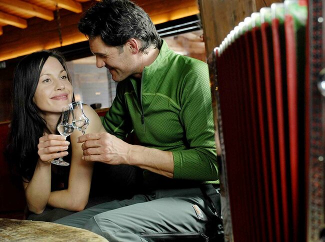 Osttiroler Pregler Ein Pärchen stoßt mit einem Osttiroler Pregler an und Vordergrund eine Ziehharmonika für ein authentisches Bild..