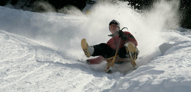 Da staubt der Pulverschnee, als der Rodler die Kurve einer Rodelbahn nimmt. Ein natürlcher Schneewall begrenzt die Bahn.