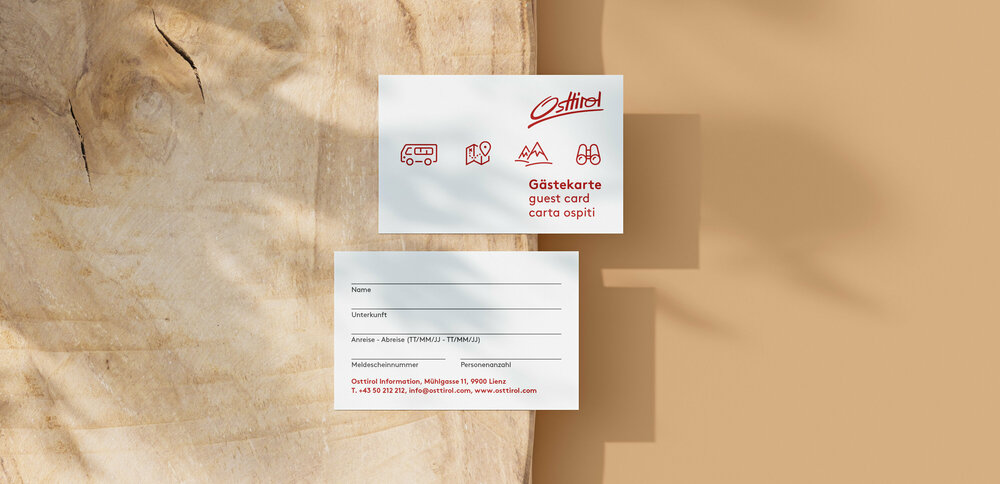 Die Osttiroler Gästecard mit roter Schrift auf weißem Papier, dahinter Holz.
